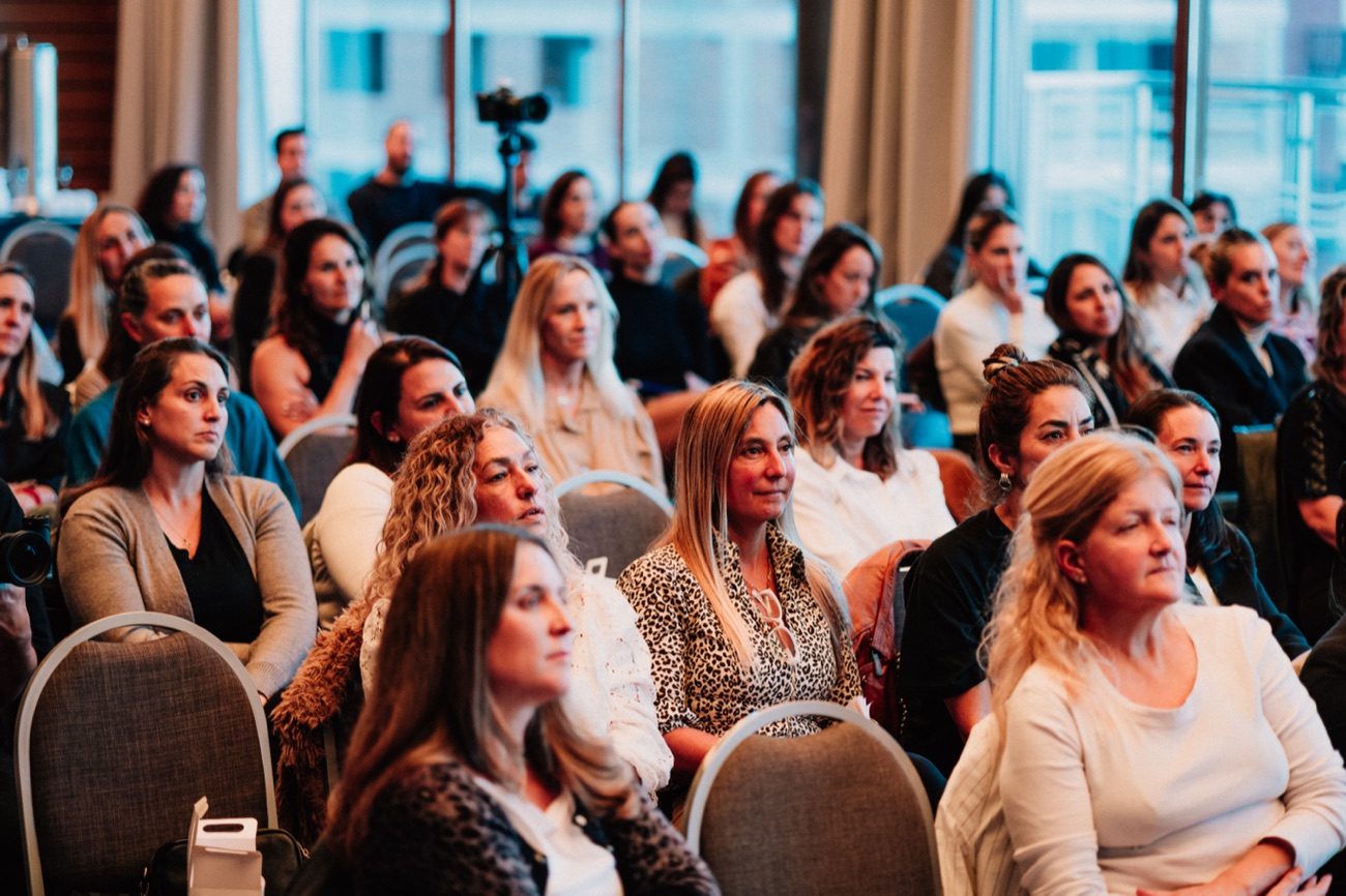 La sala llena: cuatro filas de asistentes sentadas mirando hacia el escenario